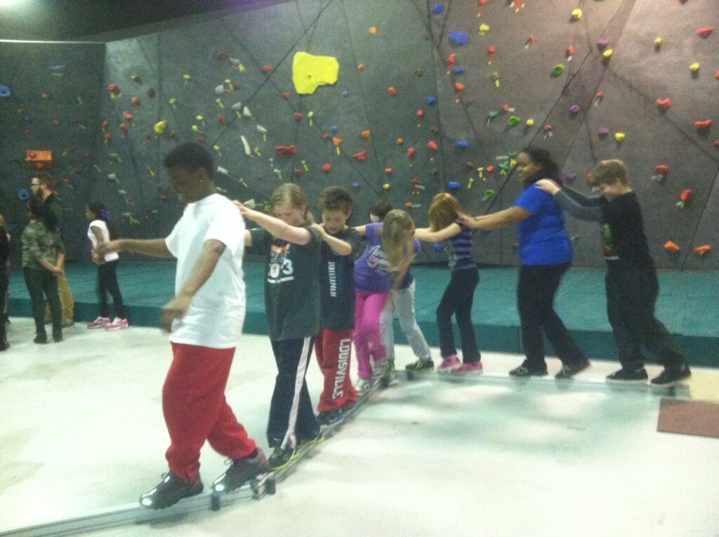 Middle school students stand on a balance beam while participating in a team building activity.