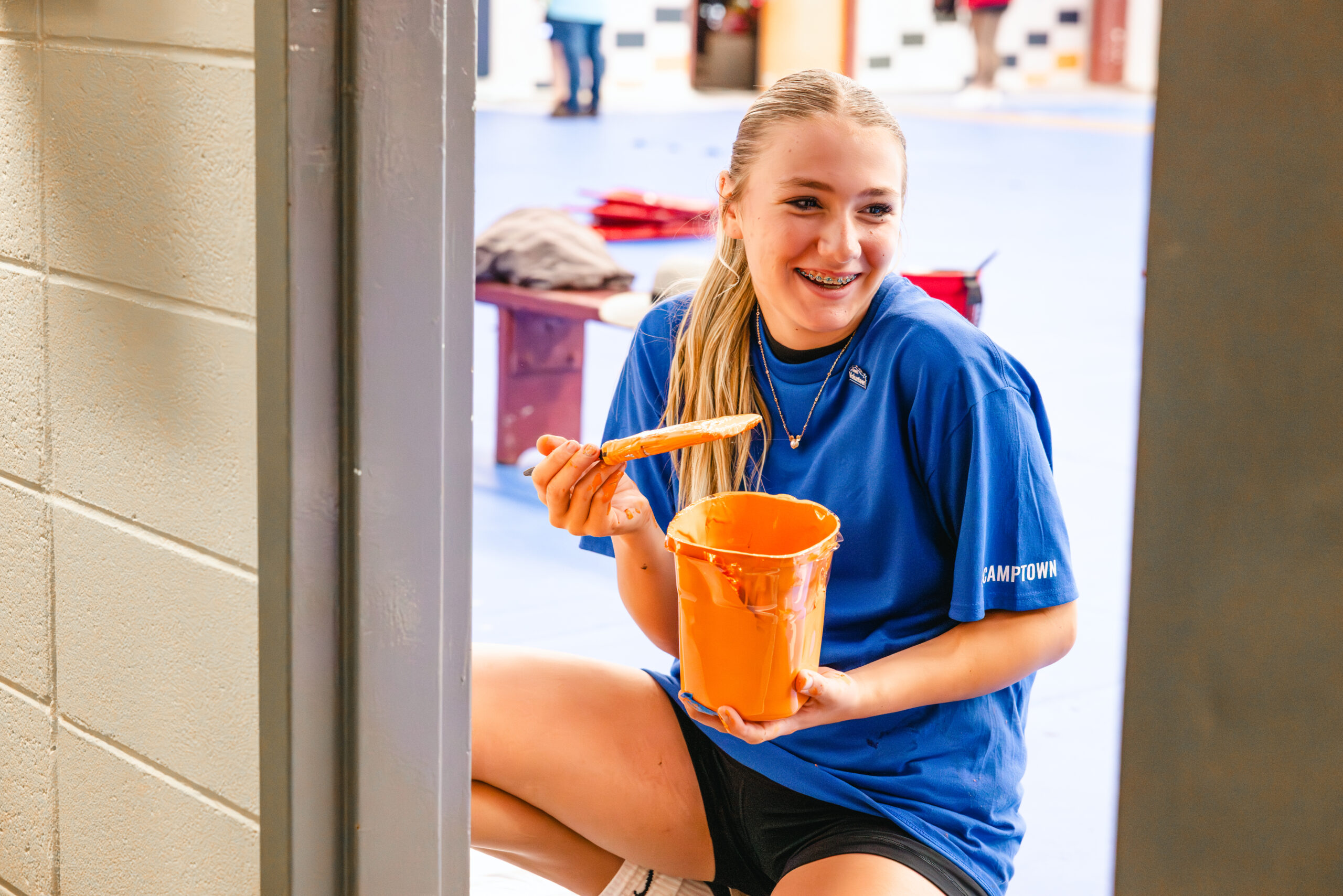Blonde girl holding paint brush and cup.