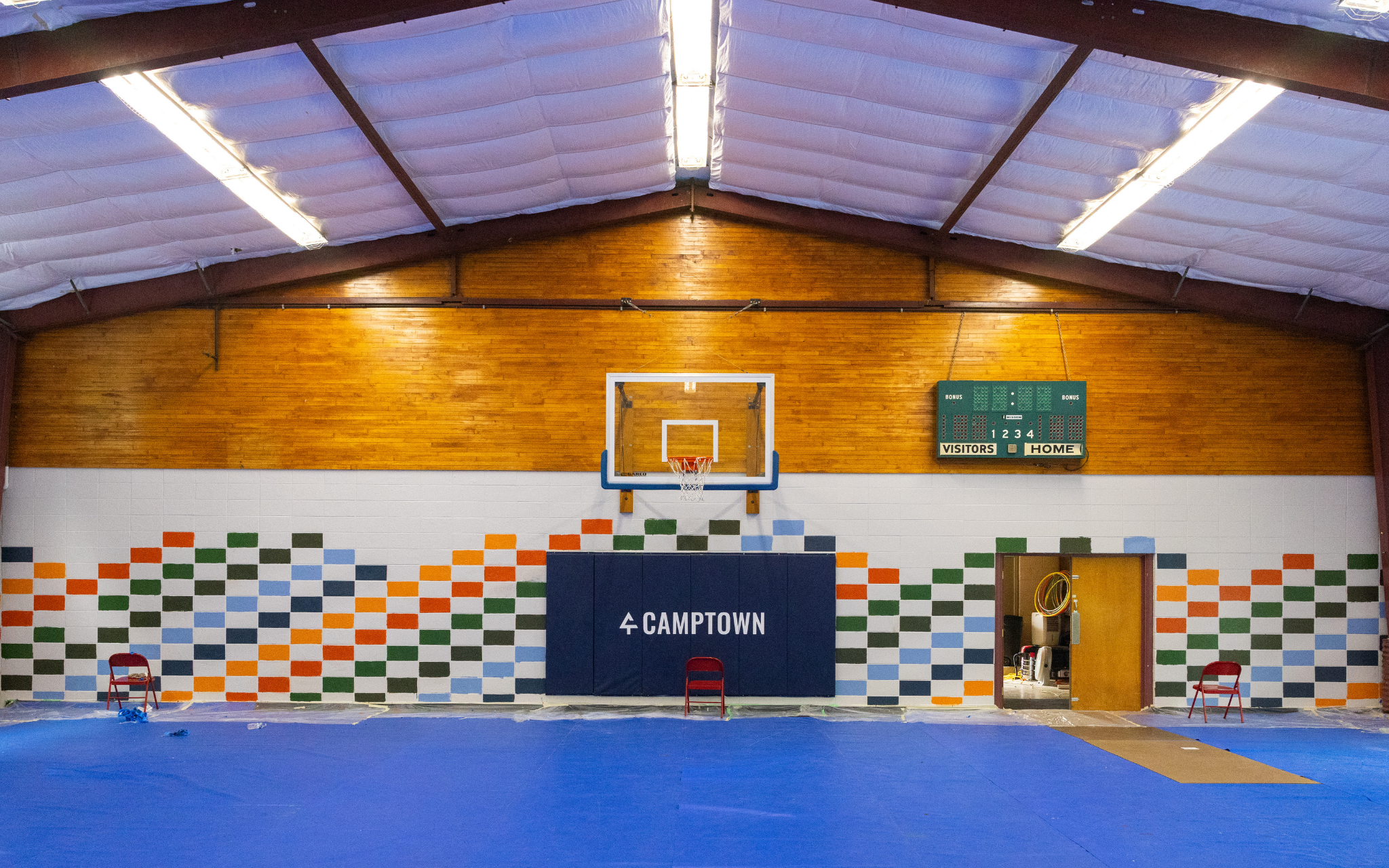 Image of a gymnasium wall with a basketball hoop, padding, and painted wall.